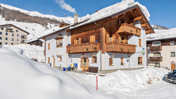 A multi-story building with wooden balconies, a snow-covered roof, and a clear blue sky.