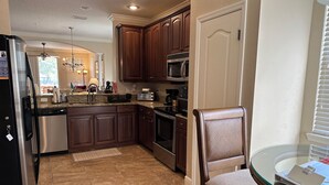 A kitchen with dark wooden cabinets, stainless steel appliances, and a glass dining table. - Luxurious River Views, Resort Amenities, Lrg 3 Bed, 2 Bath, Corner Unit, 2100 SF (Palm Coast)
