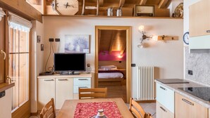 A compact room with a wooden ceiling, a bed, a TV, a dining table, and a kitchen area. - Casa Azzurra with Mountain View, Wi-Fi, Balcony & Garden; Parking Available (Livigno (SO))