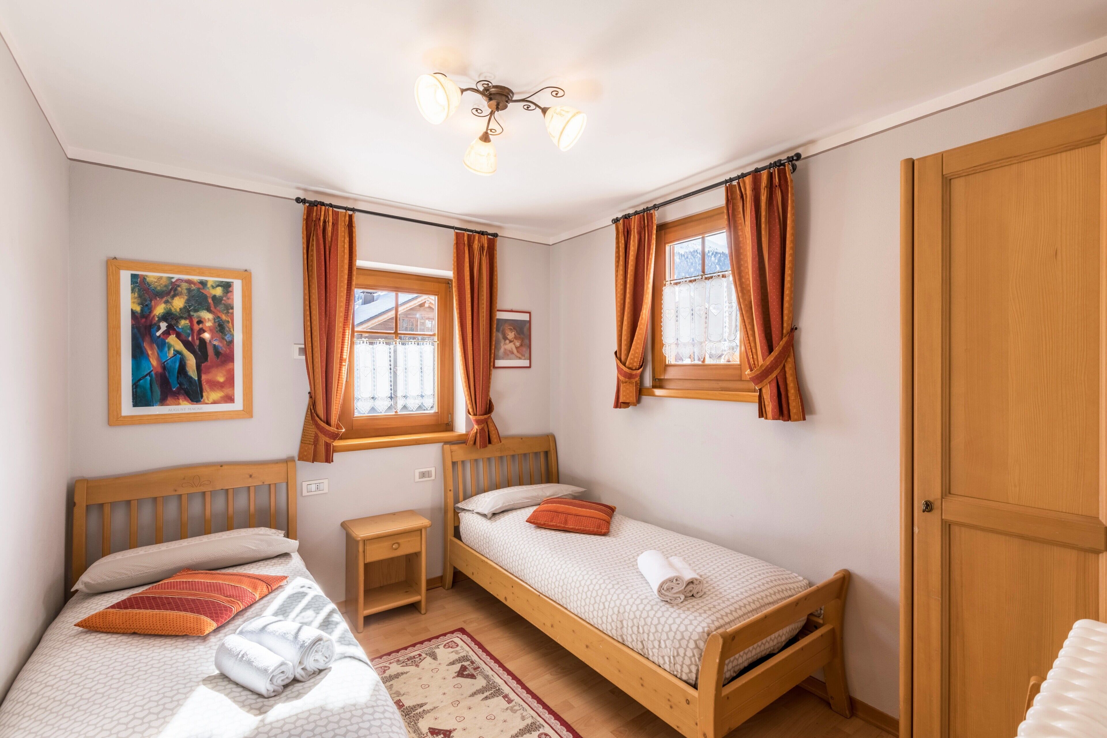 A room with two wooden beds, a small bedside table, a wall-mounted shelf, and a door.