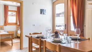 Un comedor con una mesa de madera dispuesta para cuatro personas, una mesita auxiliar y una cama al fondo.