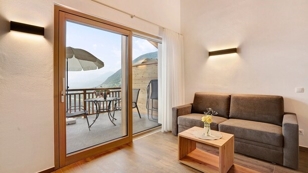 Een woonkamer met een bank, een salontafel en een schuifdeur die uitkomt op een terras met een tafel en stoelen.