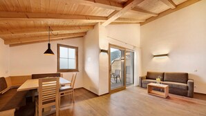 Een kamer met een houten plafond, een eettafel met stoelen, een bank en een klein bijzettafeltje.