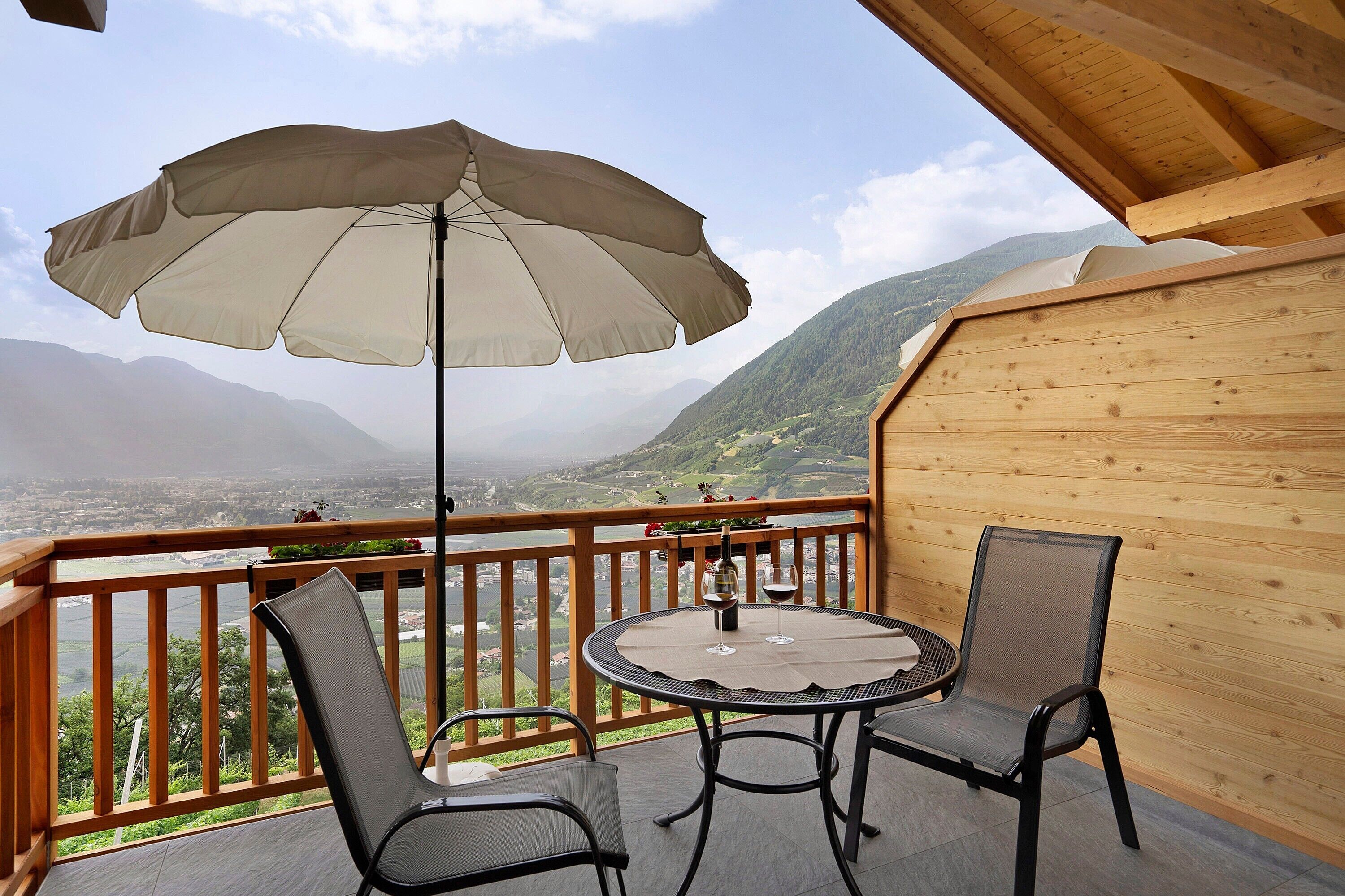 Un balcon avec une table et des chaises, un parasol et une vue sur les montagnes.
