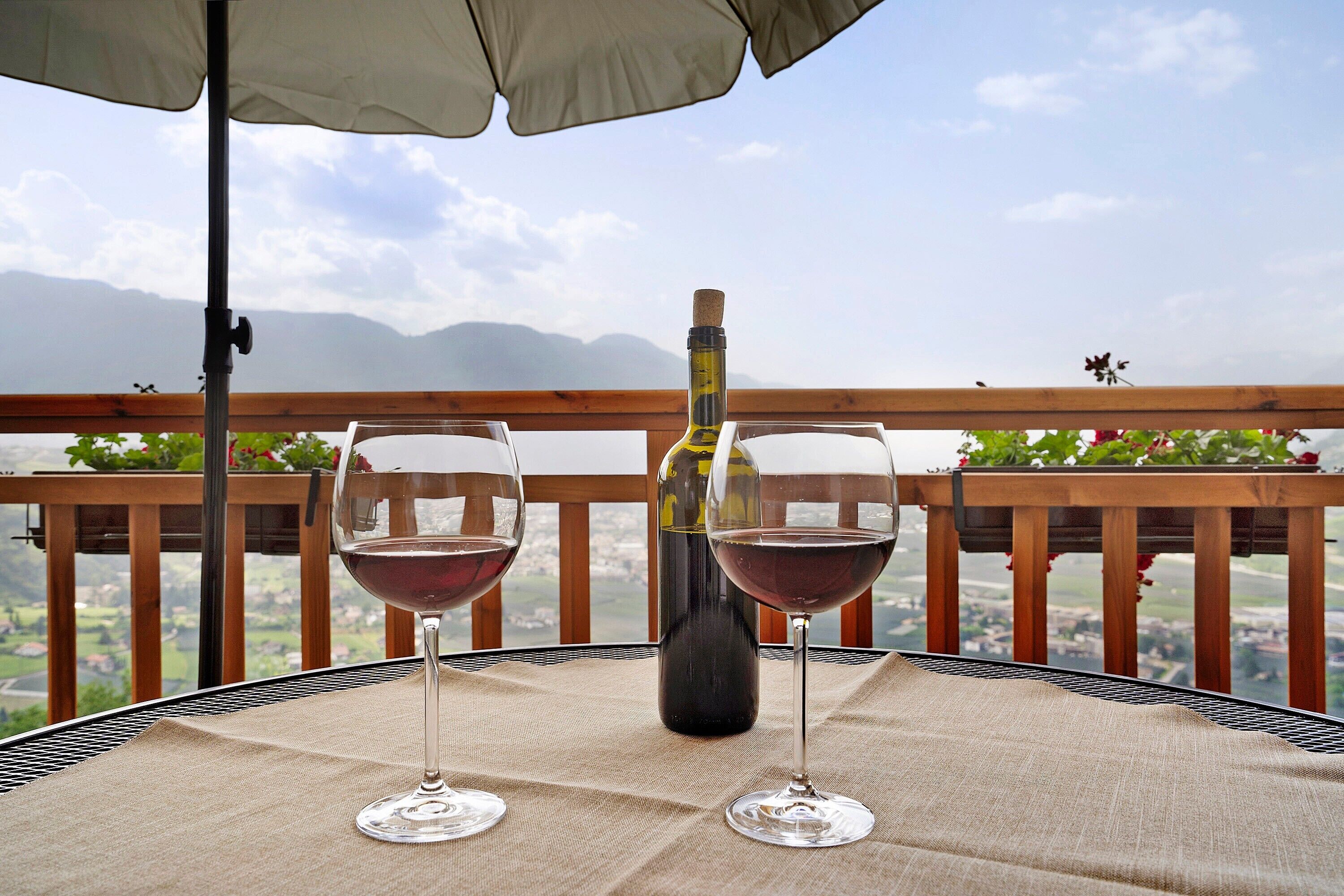 Une table avec deux verres à vin et une bouteille, placée sur un balcon donnant sur un paysage magnifique.