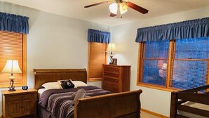 A bedroom with a wooden bed, a nightstand with a lamp, a dresser, and a window with blinds. - NEW! STUNNING Lake Harmony Mountain House Golfing! (Lake Harmony)