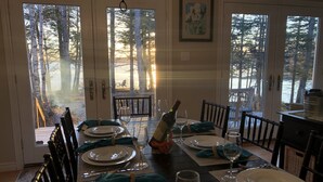 Comedor con una mesa dispuesta para cuatro, ventanas amplias con vistas a árboles y un cuadro en la pared.