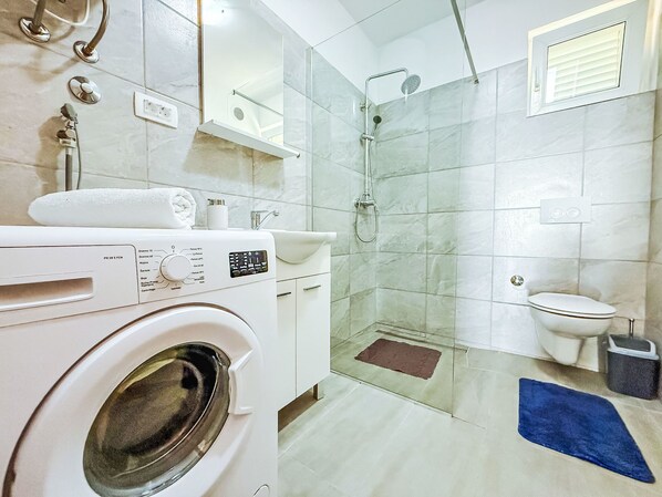 A modern bathroom with a washing machine, a glass-enclosed shower, a toilet, and a sink.