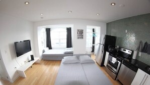 Un appartement moderne doté d’un canapé-lit, d’une télévision, d’une cuisine équipée d’une cuisinière et d’un réfrigérateur, et d’une fenêtre avec des rideaux.