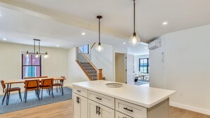 A modern kitchen with a central island, wooden dining table, and chairs. There is a staircase leading to an upper level. - Village with a View: 4 br, a/c, deck, Mansfield views! (Stowe)
