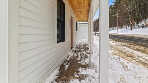 A covered porch with a wooden ceiling, a white exterior wall, and a snow-covered ground. - Village with a View: 4 br, a/c, deck, Mansfield views! (Stowe)