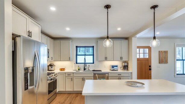 A modern kitchen with stainless steel appliances, a central island with stools, and pendant lighting. - Village with a View: 4 br, a/c, deck, Mansfield views! (Stowe)