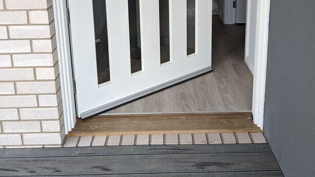 Puerta blanca con estrechas hendiduras verticales, un picaporte metálico y un umbral de madera.