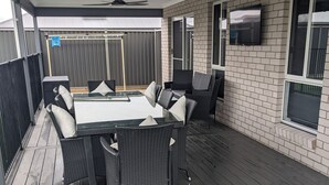 Un patio exterior con mesa y sillas, ventiladores de techo y un televisor montado en la pared.