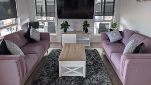 Una sala de estar moderna con dos sofás, una mesa de centro, un televisor y un mueble blanco pequeño con plantas.