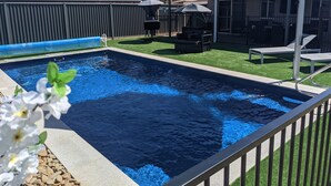 Una piscina con un deck perimetral, un espacio de descanso cubierto y un patio cercado.