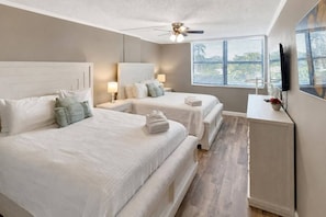 A hotel room with two beds, a ceiling fan, a TV, and a window with blinds. - Renovated 3BR Harbor Towers: Pools, Tennis & Beach (Siesta Key)
