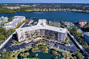A multi-story hotel with a curved roof, parking lot, and a marina with boats. - Renovated 3BR Harbor Towers: Pools, Tennis & Beach (Siesta Key)