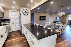 Una cocina moderna con armarios blancos, encimera de mármol negro y comedor con candelabro.