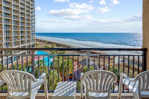 Enjoy ocean views from this balcony with a pool and building in the background.