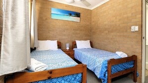 Een kamer met twee houten bedden, elk met een bedovertrek met een patroon, een nachtkastje met een lamp en een schilderij van een zandstrand aan de bakstenen muur.