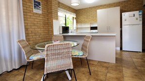Een kleine keuken met een eettafel, rieten stoelen, een koelkast en een magnetron.