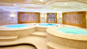 A spa area with three hot tubs arranged in a semi-circular layout, surrounded by beige-tiled steps and walls with decorative panels. - Shenyang Royal Wanxin Hotel (Shenyang)