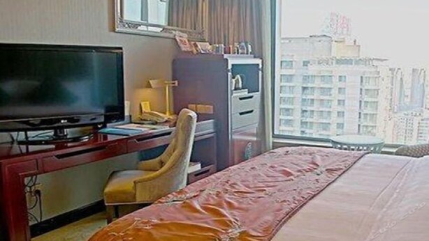 A hotel room with a bed, a desk with a computer, a chair, a television, and a window with a city view. - Shenyang Royal Wanxin Hotel (Shenyang)