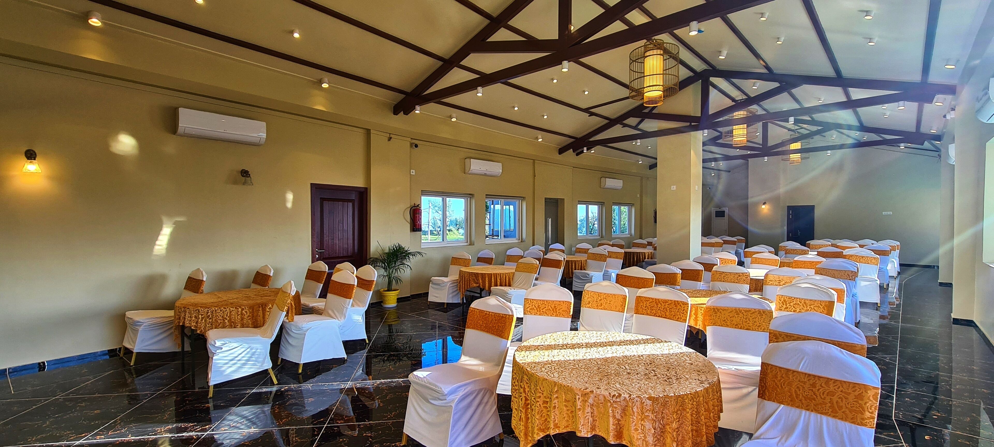 A banquet hall with rows of round tables, white tablecloths, and chairs with orange sashes.