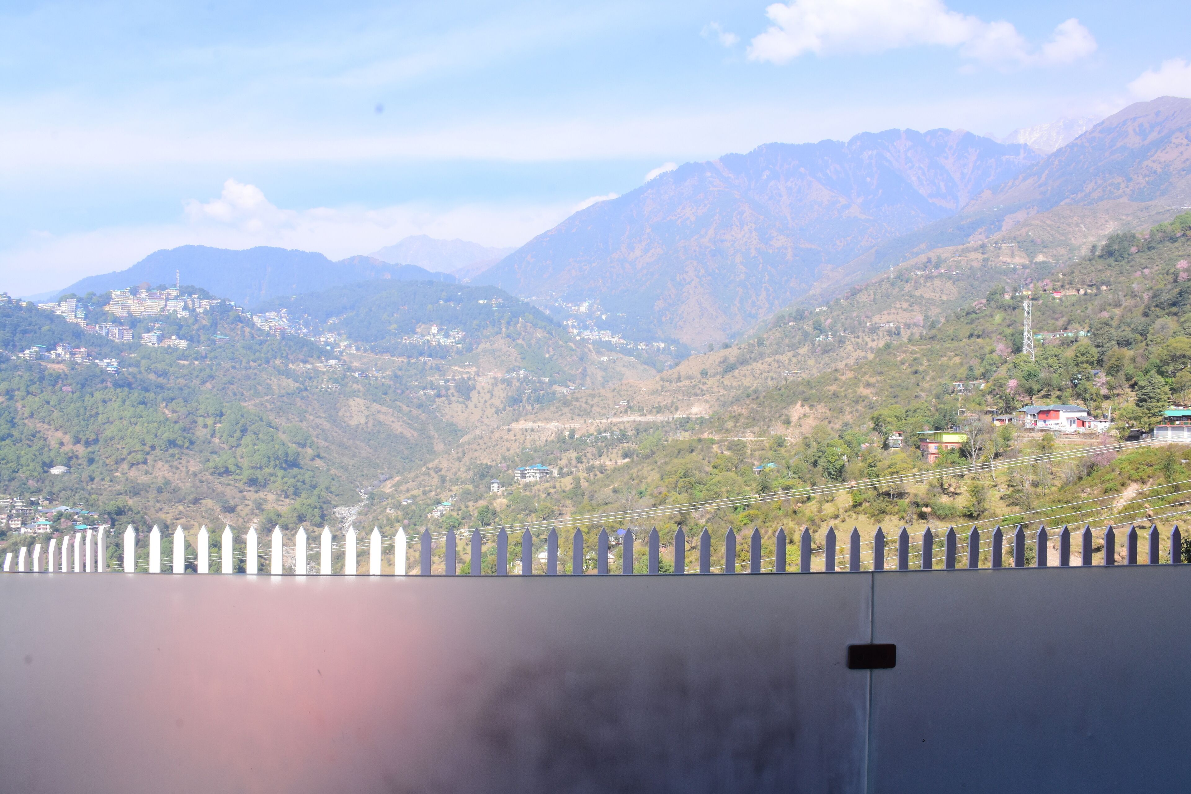 A mountainous landscape with a fence in the foreground and buildings in the background.