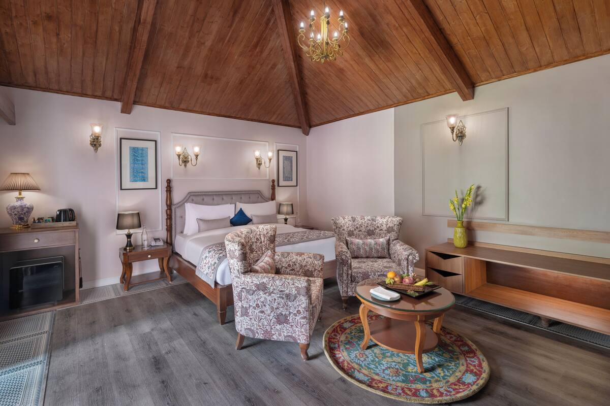 Ein geräumiges Schlafzimmer mit Holzbalkendecke, einem großen Bett, zwei Sesseln, einem runden Couchtisch und einer eingebauten Bank.