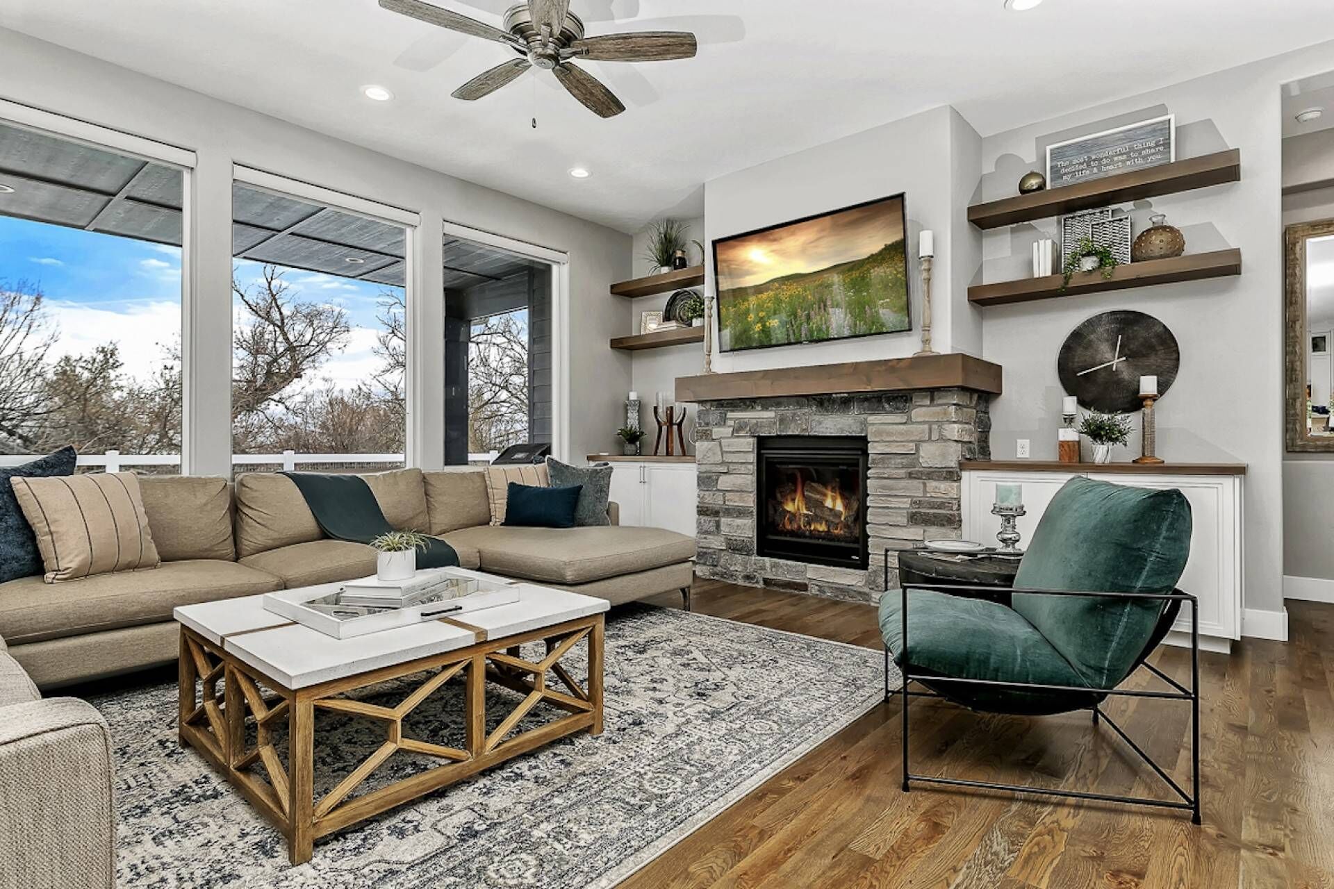 A spacious living room with a stone fireplace, large windows, and a view of the outdoors.