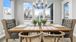 Ein Esszimmer mit Holztisch, gepolsterten Stühlen, einer Kristallleuchter und Blick auf eine verschneite Landschaft durch große Fenster.