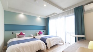 A hotel room with two beds, a small table, and a window with curtains. - Blue Cove Terrace (Miyakojima)