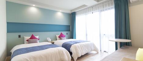 A hotel room with two beds, a small table, and a window with curtains.