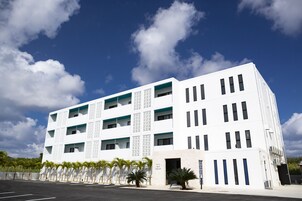 Un edificio moderno de varios pisos con fachada blanca, múltiples balcones y un estacionamiento con palmeras.