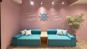 A teal sofa with a wooden table in the center, a wall with a nautical wheel and text, and a potted plant. - Blue Cove Terrace (Miyakojima)