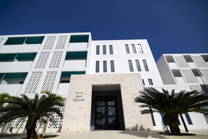 A modern building with a white facade, a central entrance, and palm trees in the foreground. - Blue Cove Terrace (Miyakojima)