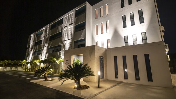 A modern building with a flat facade, multiple balconies, and a well-lit entrance. - Blue Cove Terrace (Miyakojima)