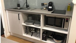 A compact kitchenette with a sink, microwave, and storage shelves.