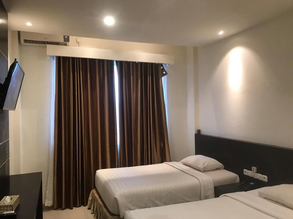 Une chambre d’hôtel avec deux lits, un téléviseur sur le côté gauche et un rideau qui recouvre la fenêtre.