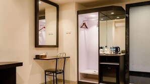 Une chambre d’hôtel compacte comprenant un miroir, une chaise, une petite table, un espace douche et un mini-réfrigérateur.