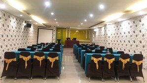 Une salle de conférence avec des rangées de tables et de chaises, un pupitre et un écran à l’avant.