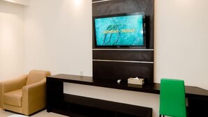 Un salon moderne avec un téléviseur à écran plat fixé sur un mur noir, un fauteuil beige, une chaise verte et un meuble de rangement noir.