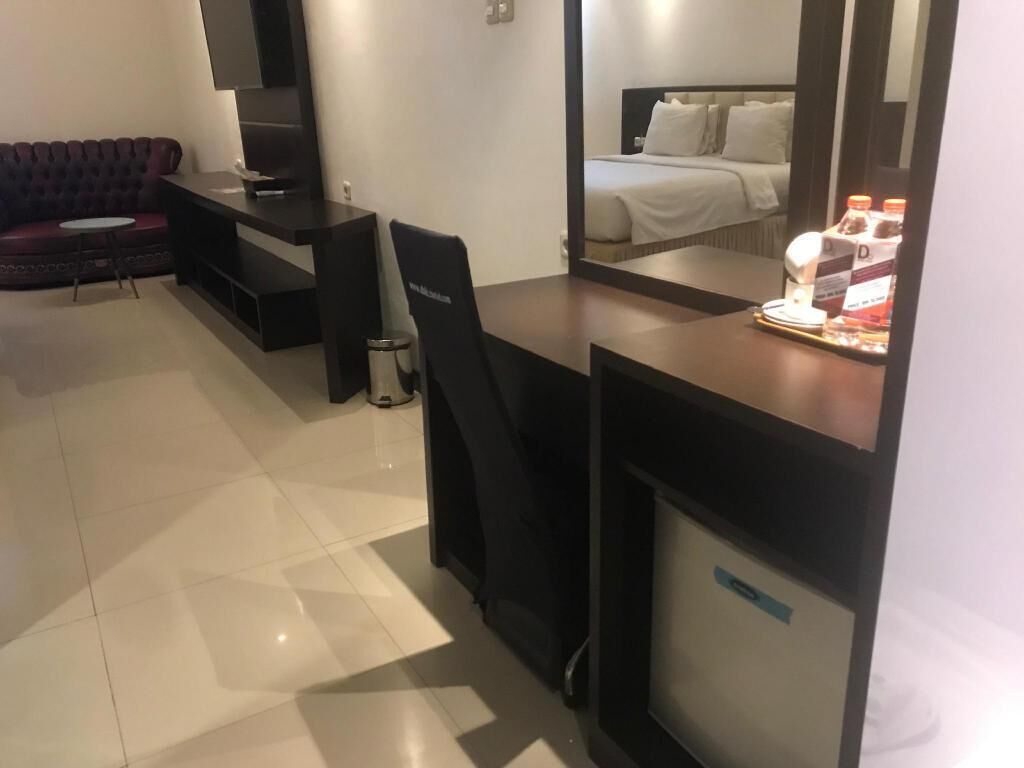 A hotel room with a bed, a desk with a chair, a small table, and a mirror.