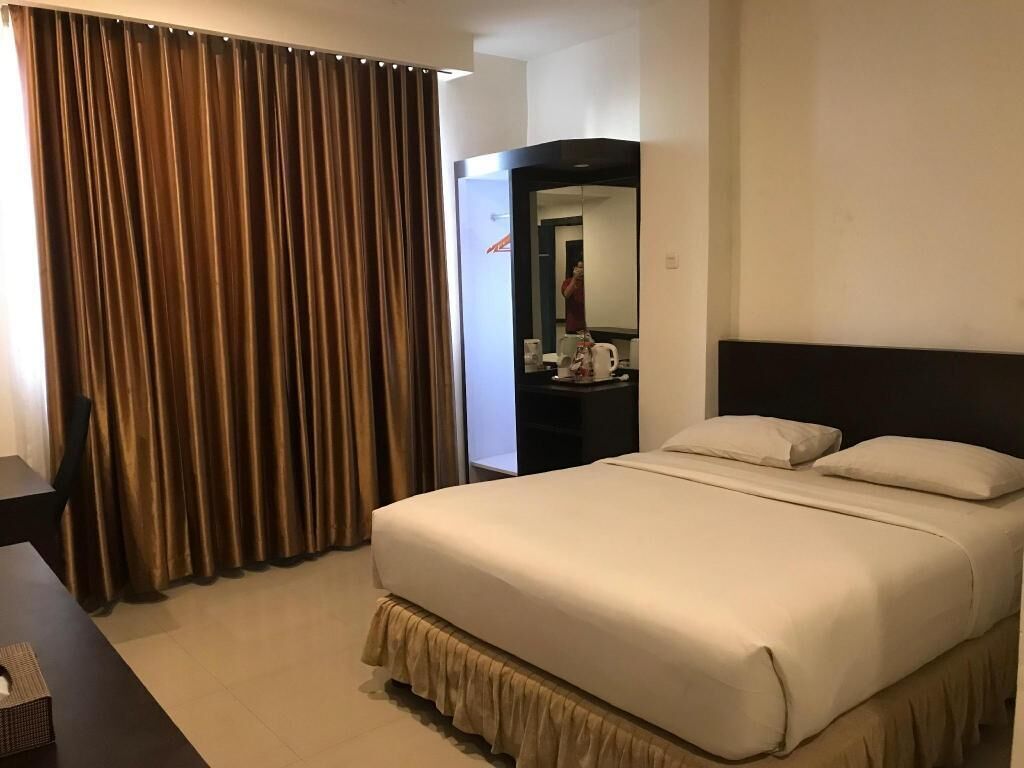 A hotel room with a large bed, a bedside table, a mirror, and a curtain.