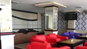 Un hall d’hôtel moderne avec des sièges rouges et violets, un grand miroir et un téléviseur à écran plat fixé au mur.