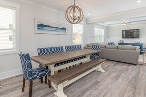 Un comedor con mesa de madera y bancos, un sofá y una araña.