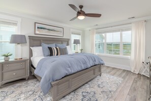 Une chambre à coucher avec un lit, des tables de chevet, un ventilateur de plafond et de grandes fenêtres.