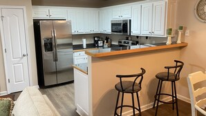 A kitchen with white cabinets, a stainless steel refrigerator, a microwave, and a wooden island with two stools. - Charming, Stylish and Cozy 3 Bedroom Townhouse near Athens (Winder)